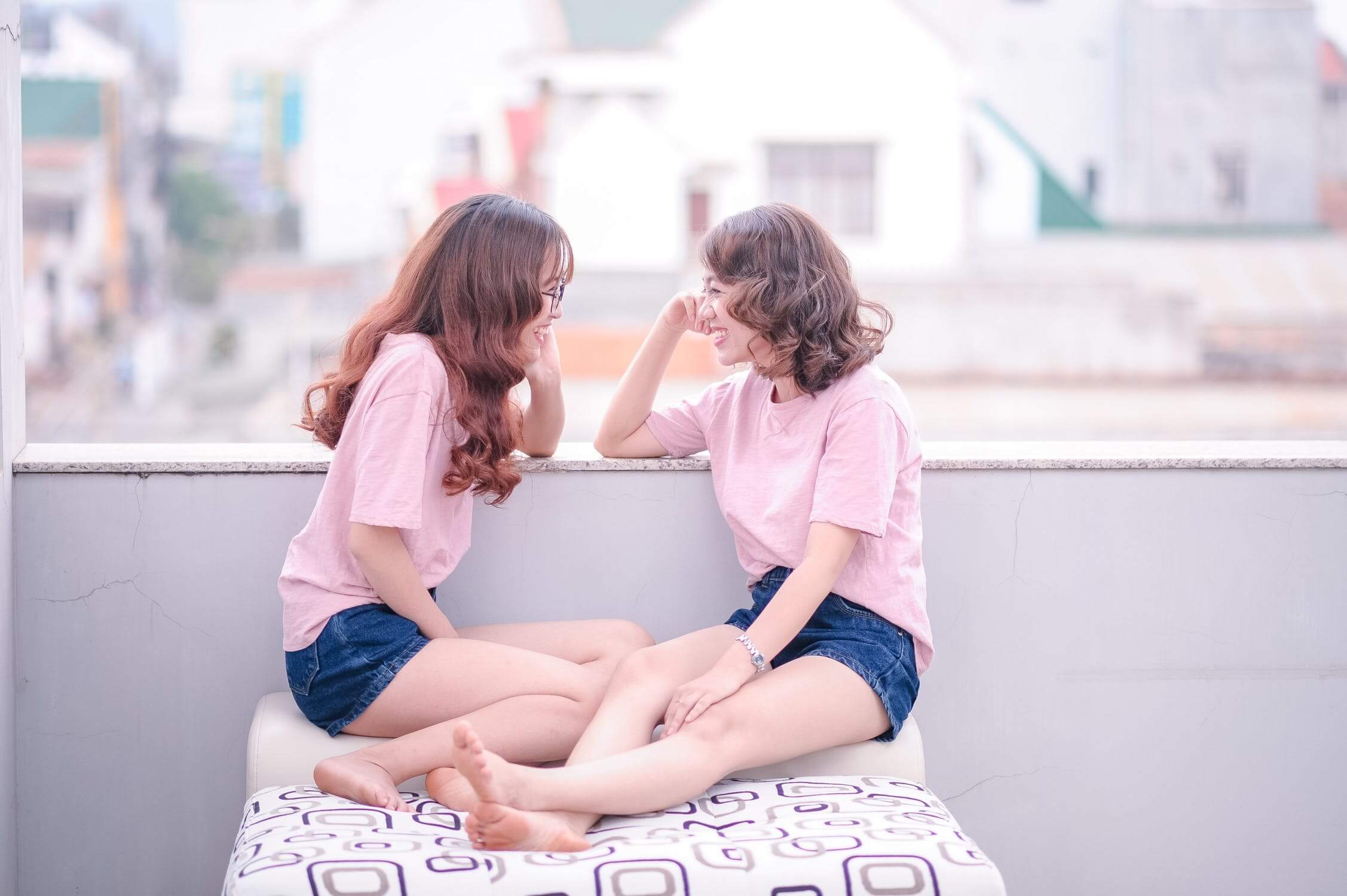 Two female identical twins sit on a rooftop and smile at each other