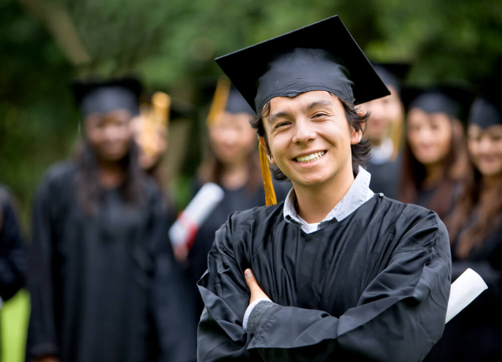 Student who took advantage of the 529 Plan tax deduction smiles as he wears black graduation gowns at his graduation ceremony