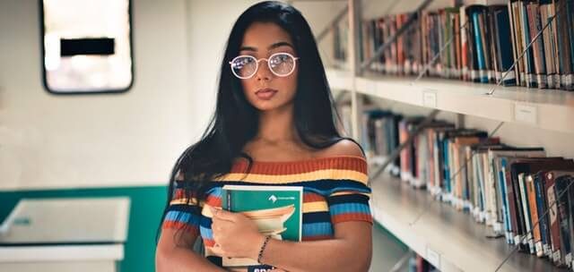 High school sophomore stands with books in a library
