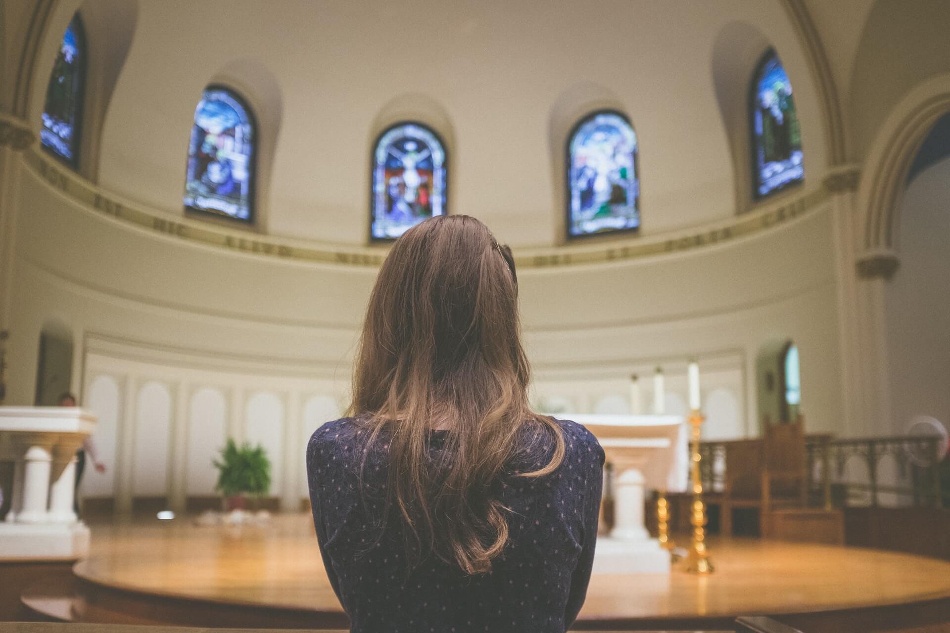 Catholic scholarship recipient stands in a church and looks at stained glass windows