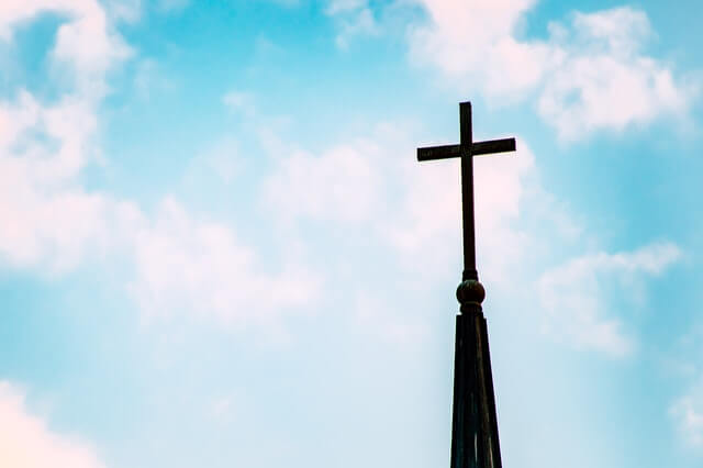Cross sitting on top of a Christian Church with a blue sky in the background