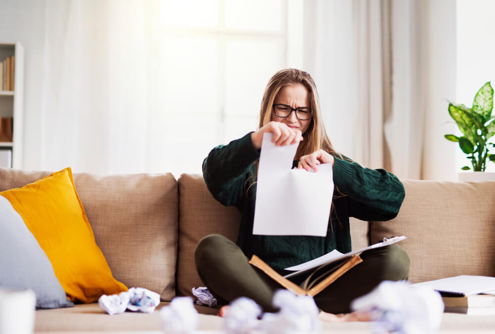 Woman sitting on a couch rips apart her essay when she realizes she doesn't need it to apply for these scholarships