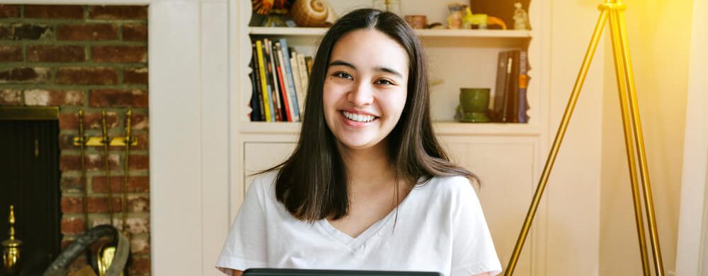 Homeschooling student studies on her laptop and smiles at the camera